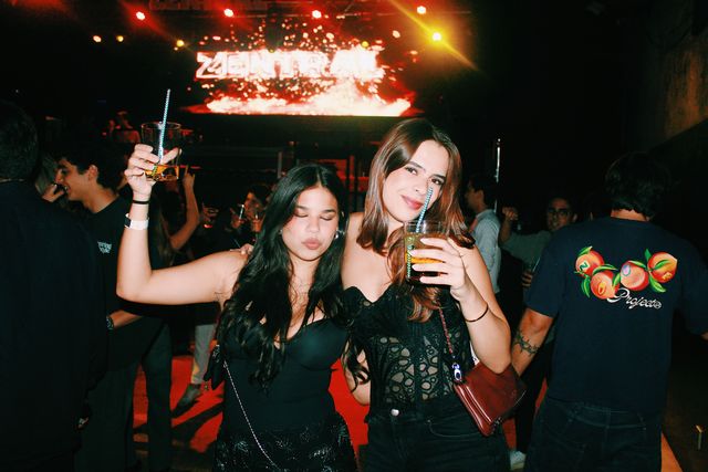 Dos chicas posan bajo la pantalla de Zentral: una levanta su vaso con los ojos cerrados y morritos y la otra, con top negro de encaje, mira a cámara.