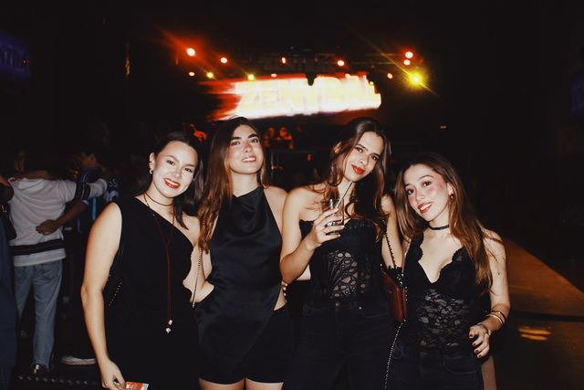 Cuatro chicas vestidas de negro posan juntas y sonríen a cámara, una con un vaso en la mano, bajo la pantalla luminosa de Zentral y varios focos.