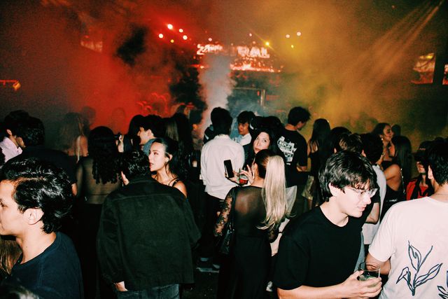La multitud llena la pista entre humo rojo y amarillo, con el letrero de Zentral al fondo y un chico con gafas y un vaso en primer plano.