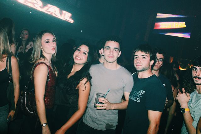 Dos chicas y dos chicos posan con el letrero de Zentral al fondo; la del top rojo pone morritos, la otra sonríe y un chico de camiseta gris sujeta un vaso.