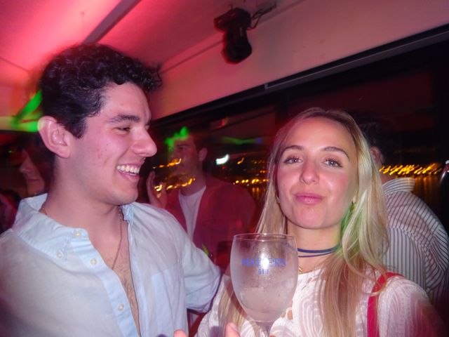 Un chico se ríe a carcajadas junto a una chica rubia que hace morritos con una copa en la mano, entre luces rosas y verdes.