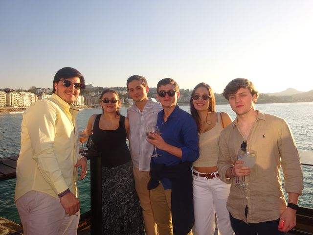 Un grupo de dos chicas y cuatro chicos mira a cámara con copas en la mano, con la costa y el mar de fondo al atardecer.