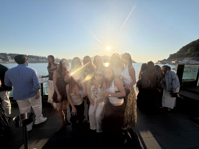 Un grupo grande de chicas posa en una terraza frente al mar, a contraluz del sol bajo, que deja destellos de luz sobre ellas.