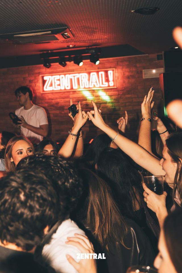 El público baila con los brazos en alto bajo el neón rojo de Zentral, con un chico de camiseta blanca al fondo.