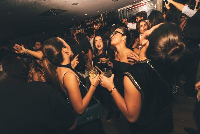 Un grupo de chicas baila y ríe con las copas en la mano, entre la multitud.