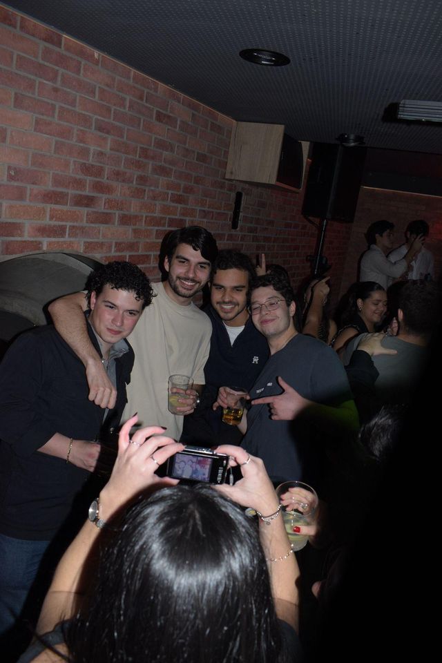 Un grupo de chicos posa abrazado junto a la pared de ladrillo mientras una chica, en primer plano, les hace una foto.
