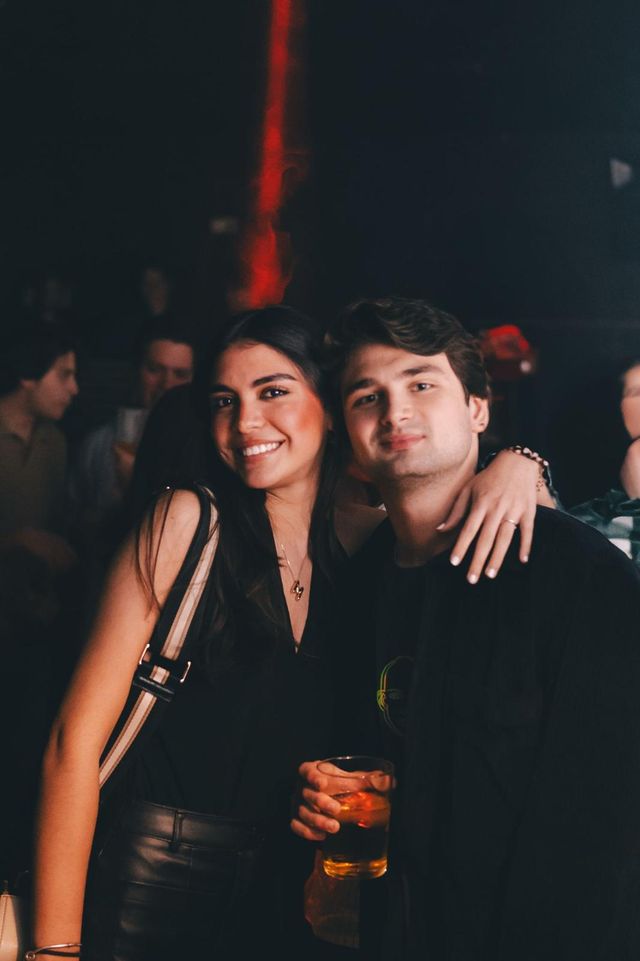 Una pareja posa abrazada entre la gente, con una luz roja vertical detrás.