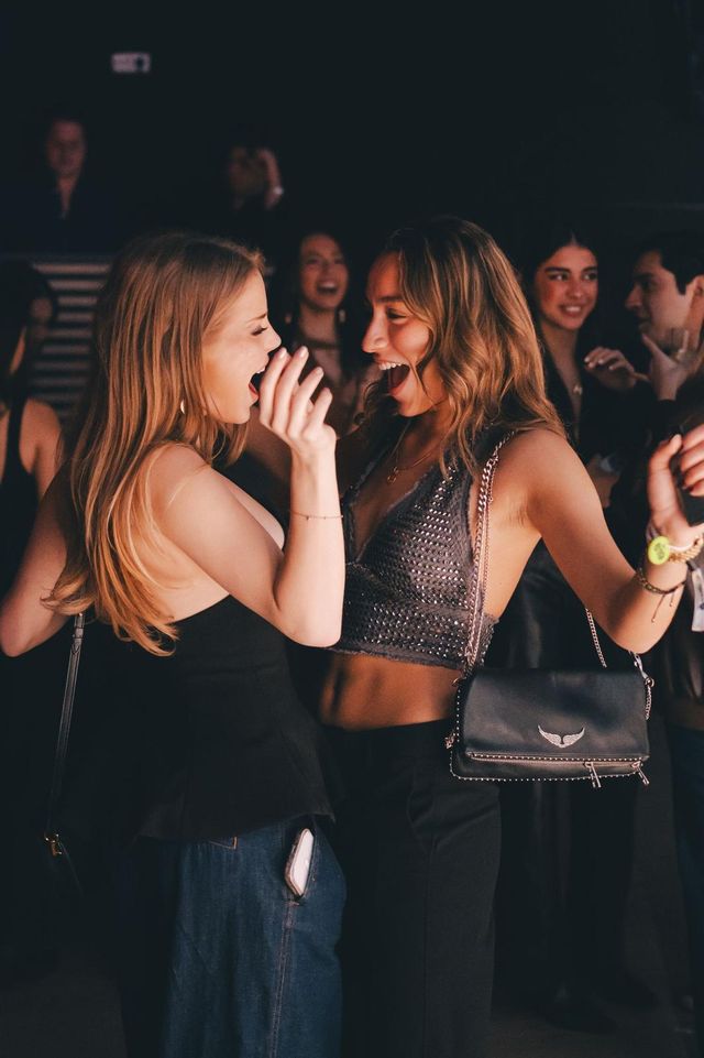 Dos amigas bailan juntas riendo, rodeadas de gente en la pista.