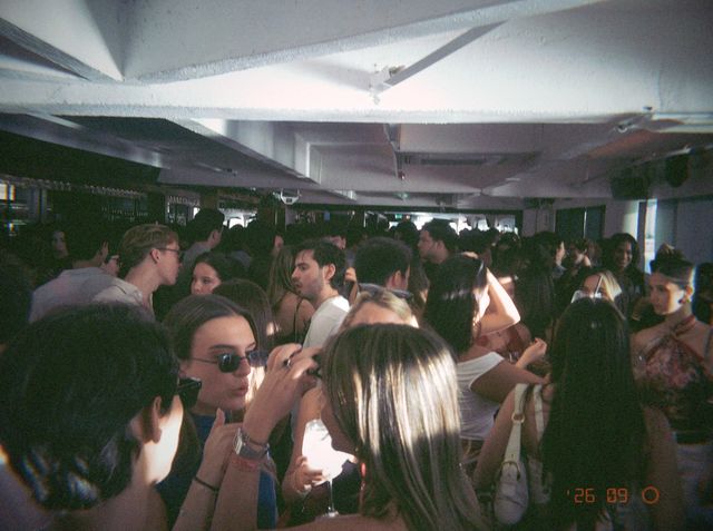 Una chica con gafas de sol charla en la sala abarrotada mientras un rayo de sol ilumina el pelo de su amiga.