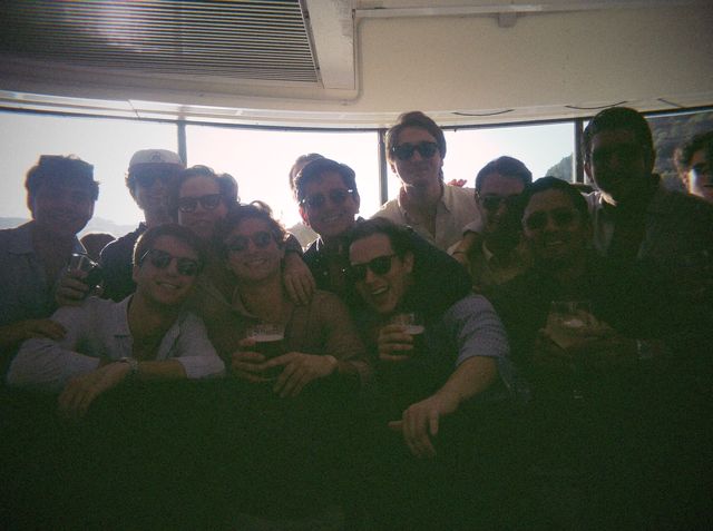 Una docena de chicos, casi todos con gafas de sol, se apiñan con cervezas a contraluz ante los ventanales.