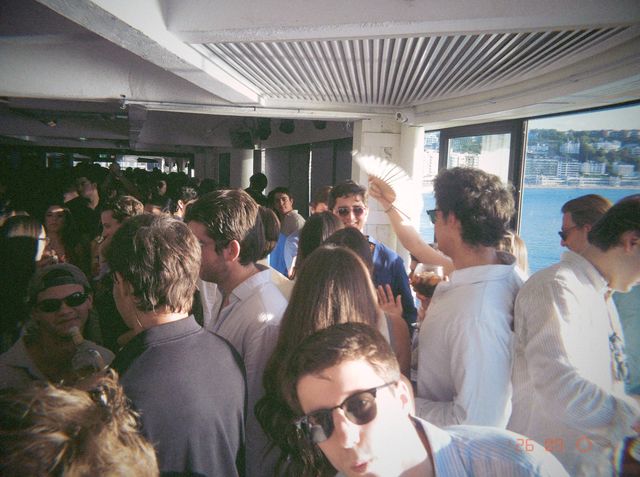 Alguien levanta un abanico blanco entre la gente apiñada junto a los ventanales que dan a la bahía.