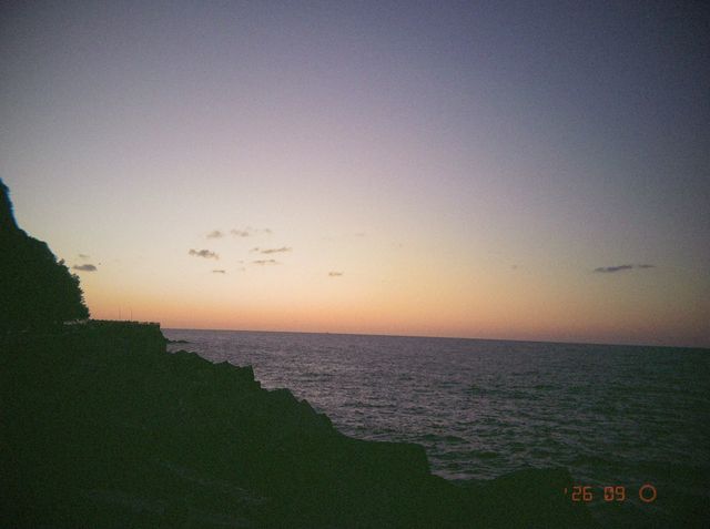 El cielo se tiñe de naranja sobre el mar tras la puesta de sol, con las rocas en silueta a la izquierda.