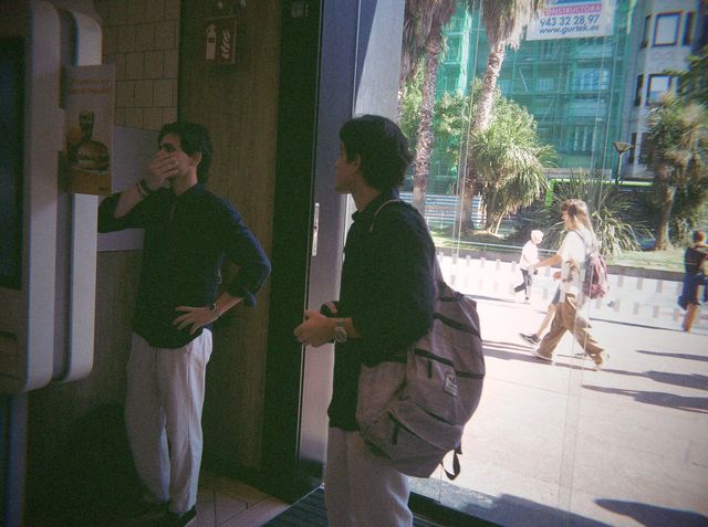 Dos chicos esperan ante la pantalla de pedidos de un local de comida rápida; uno se tapa la boca con la mano.