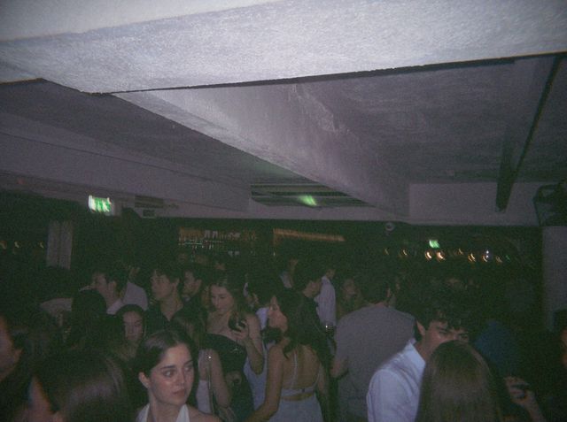 La gente llena la pista a oscuras; delante, una chica con un top blanco atado al cuello mira a un lado.