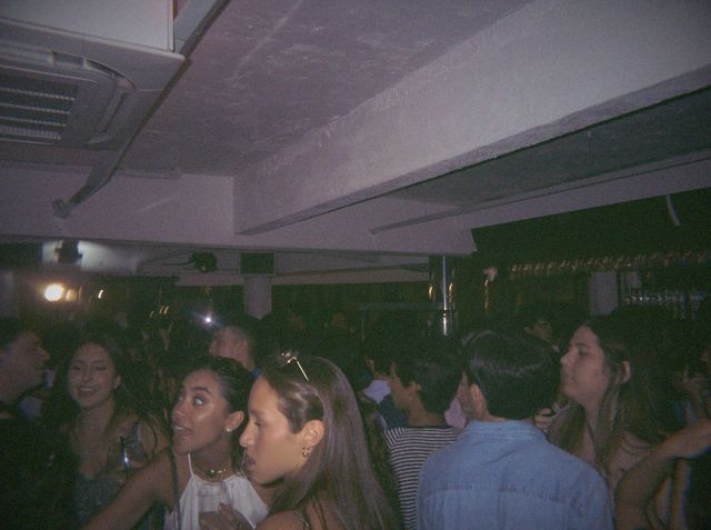 Unas chicas miran a un lado en la pista abarrotada; la de delante lleva unas gafas de sol sobre la cabeza.
