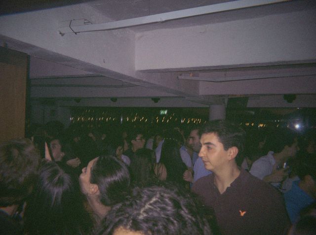 Un chico con polo oscuro mira de reojo entre la multitud apretada, con luces de la ciudad tras los cristales.